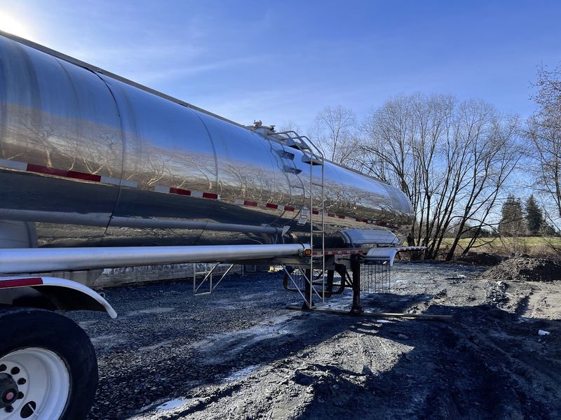 Side view of the polished stainless tank with its ladder, bare trees behind.